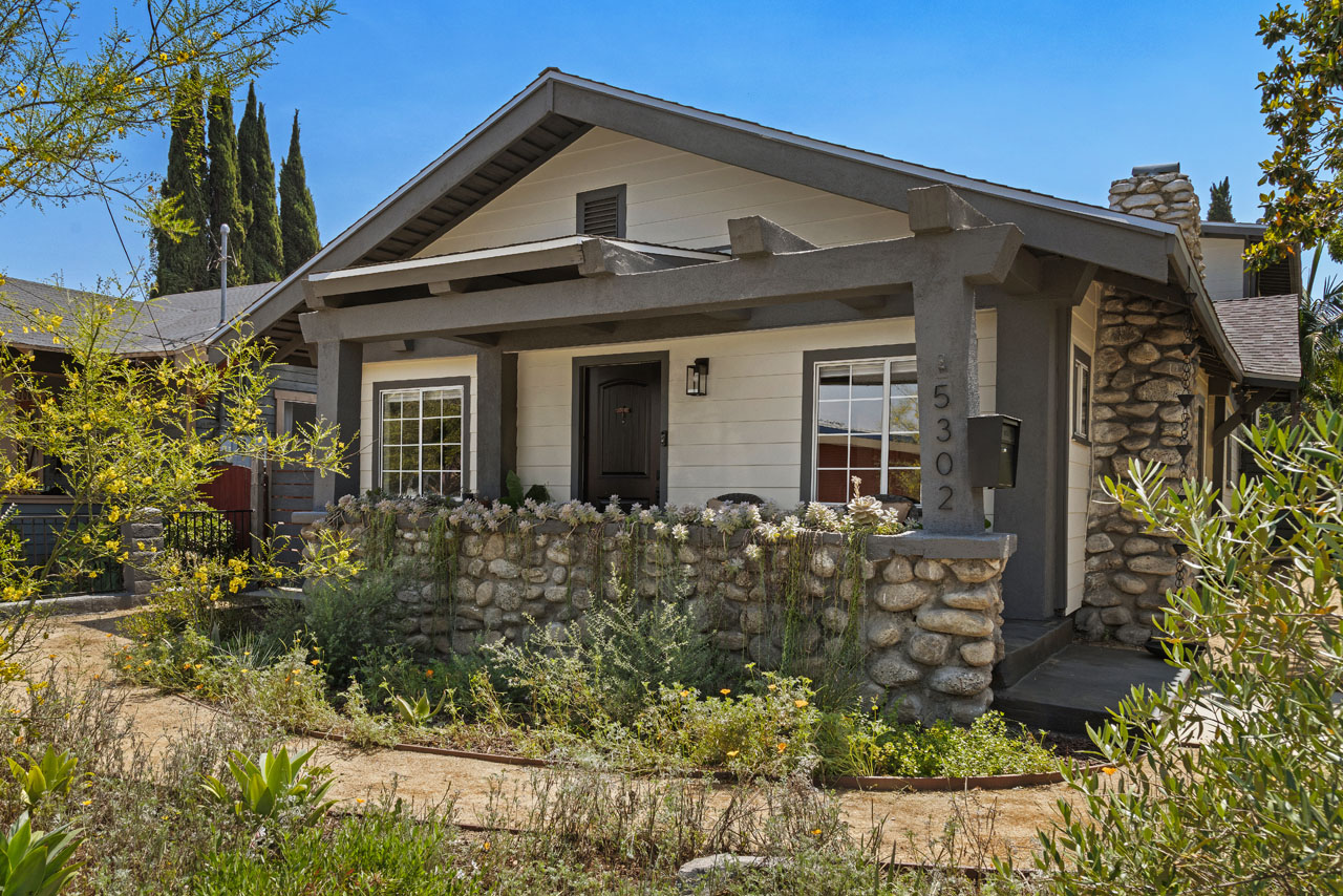 exterior of a craftsman bungalow style home, painted light yellow with deep blue trim