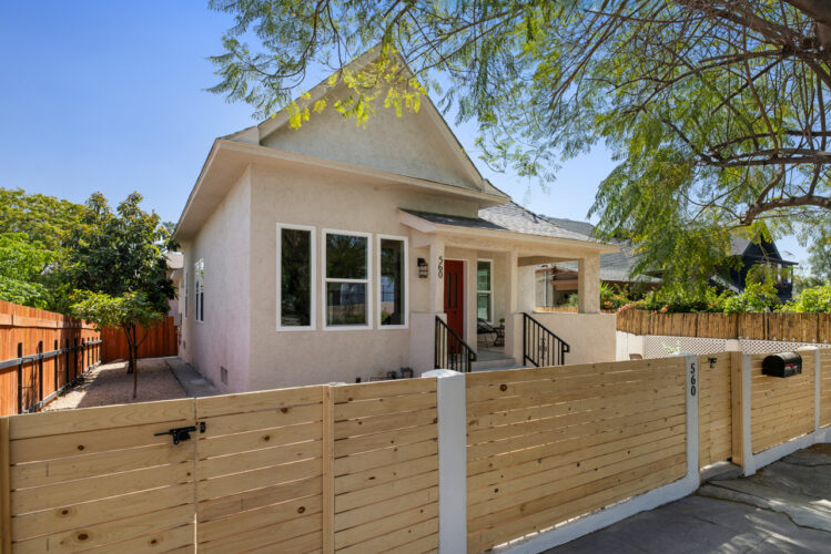 exterior of a traditional home painted white pink with a wood fence and tree
