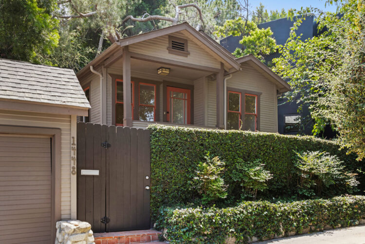 exterior of a bungalow home painted multiple shades of green with red details and a green hedge and garage