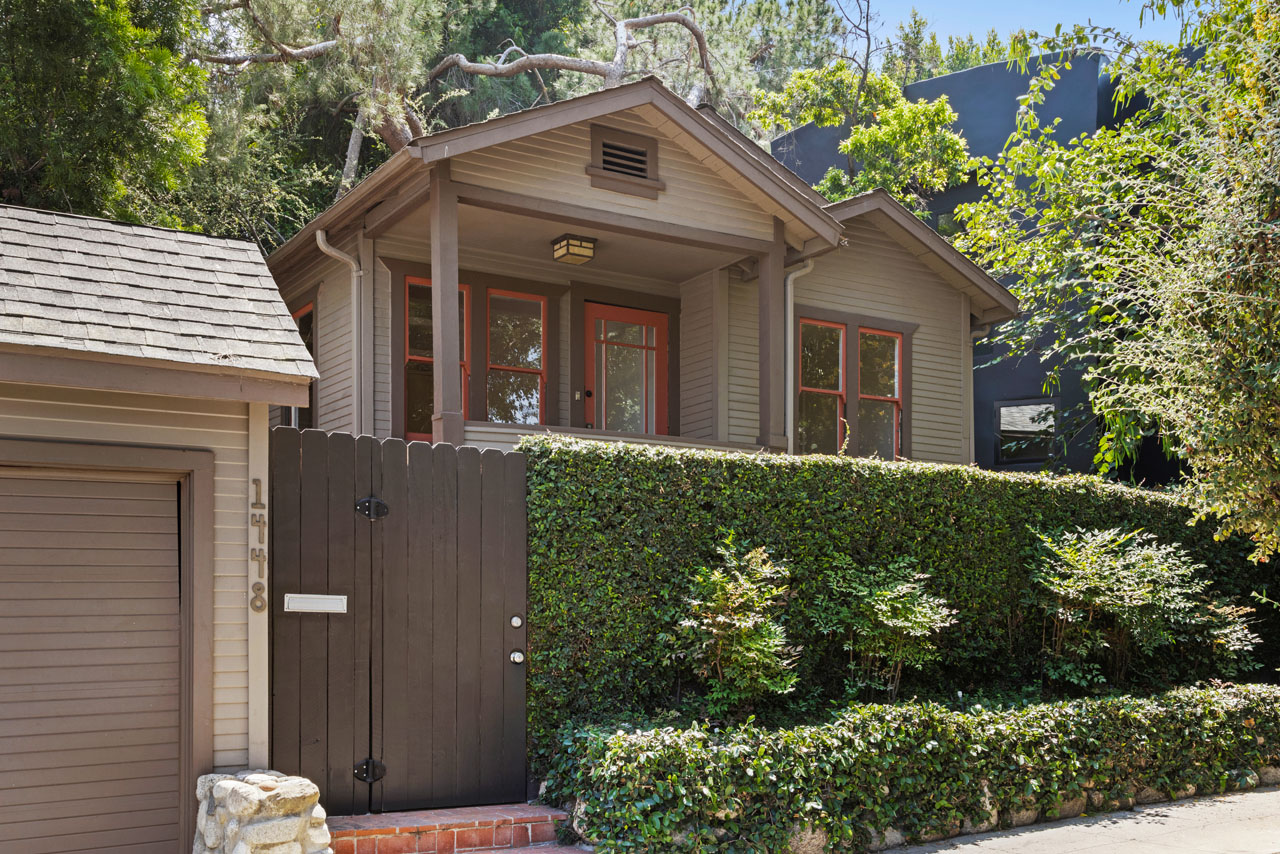 exterior of a bungalow home painted multiple shades of green with red details and a green hedge and garage