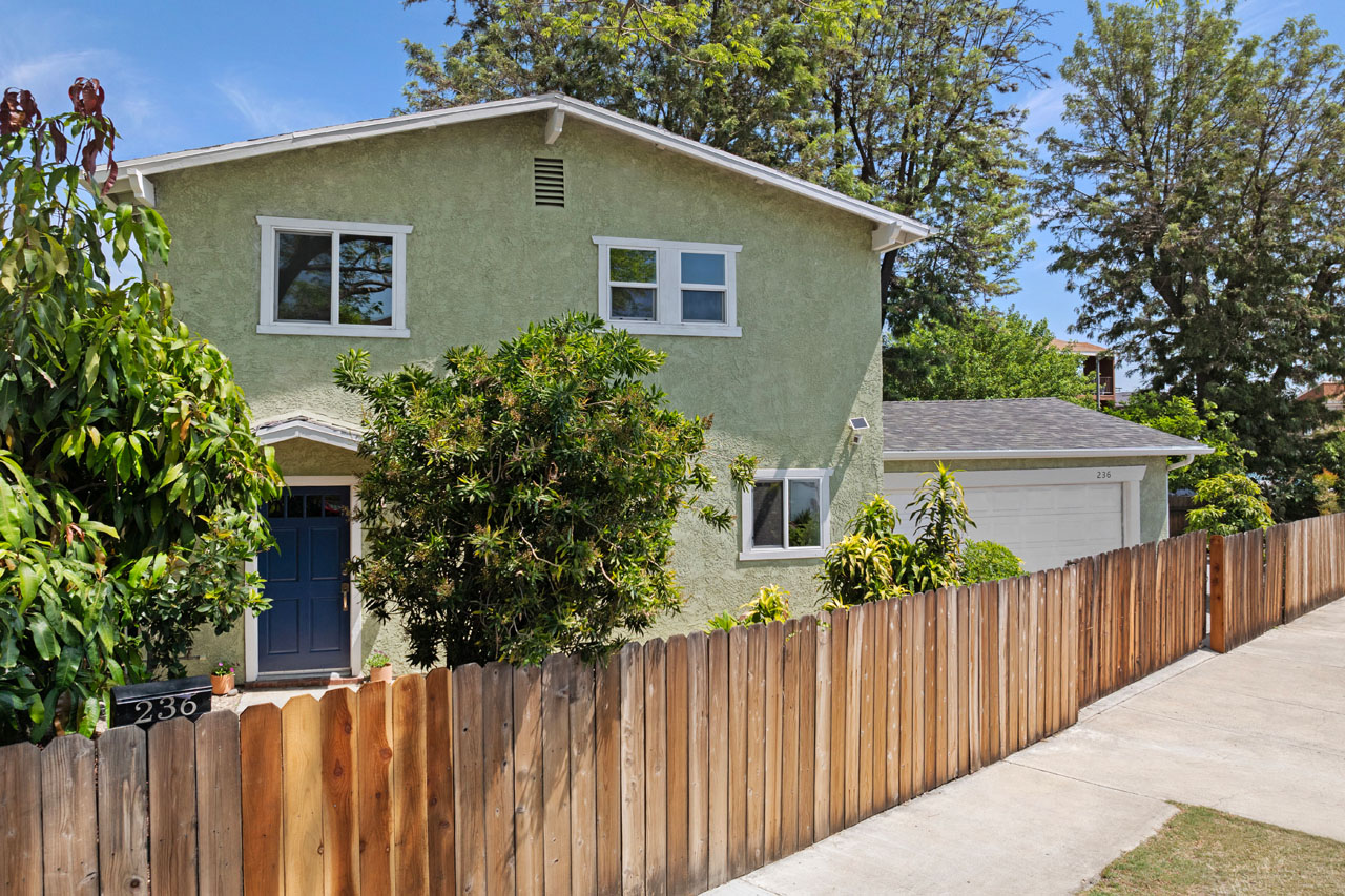 exterior of a green two story house with a wooden fence