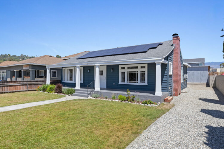 exterior of a one story traditional home painted blue with a front porch, white columns and colar panels on the roof