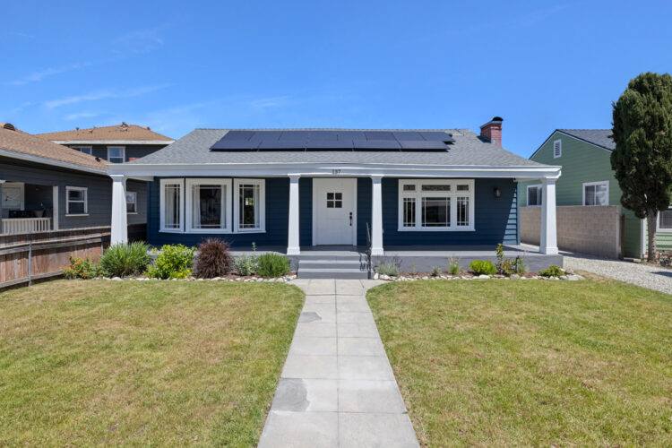 exterior of a one story traditional home painted blue with a front porch, white columns and colar panels on the roof