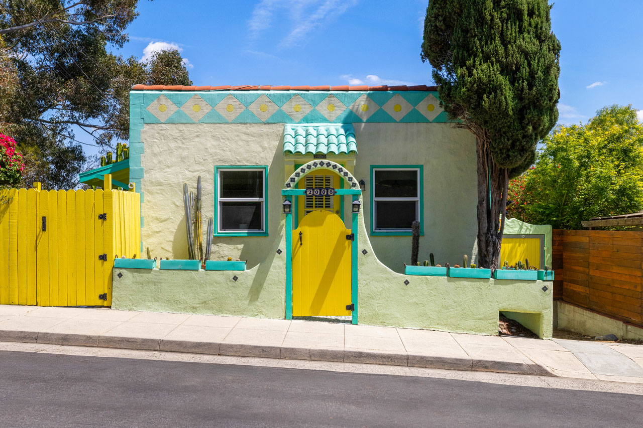 exterior of a spanish style casita home painted bright yellow and aqua with a yellow fence and green cypress