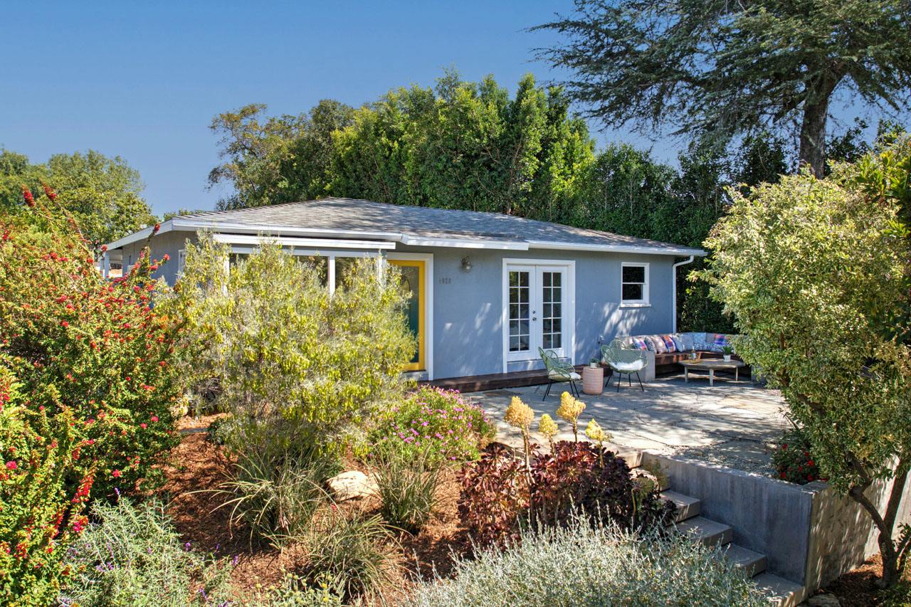 exterior of a one story home painted blue with yellow door and verdant california native landscaping