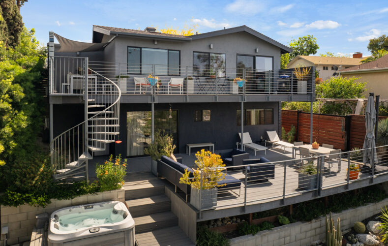 back view of a two story mid century home painted in greys with spiral staircase and jacuzzi