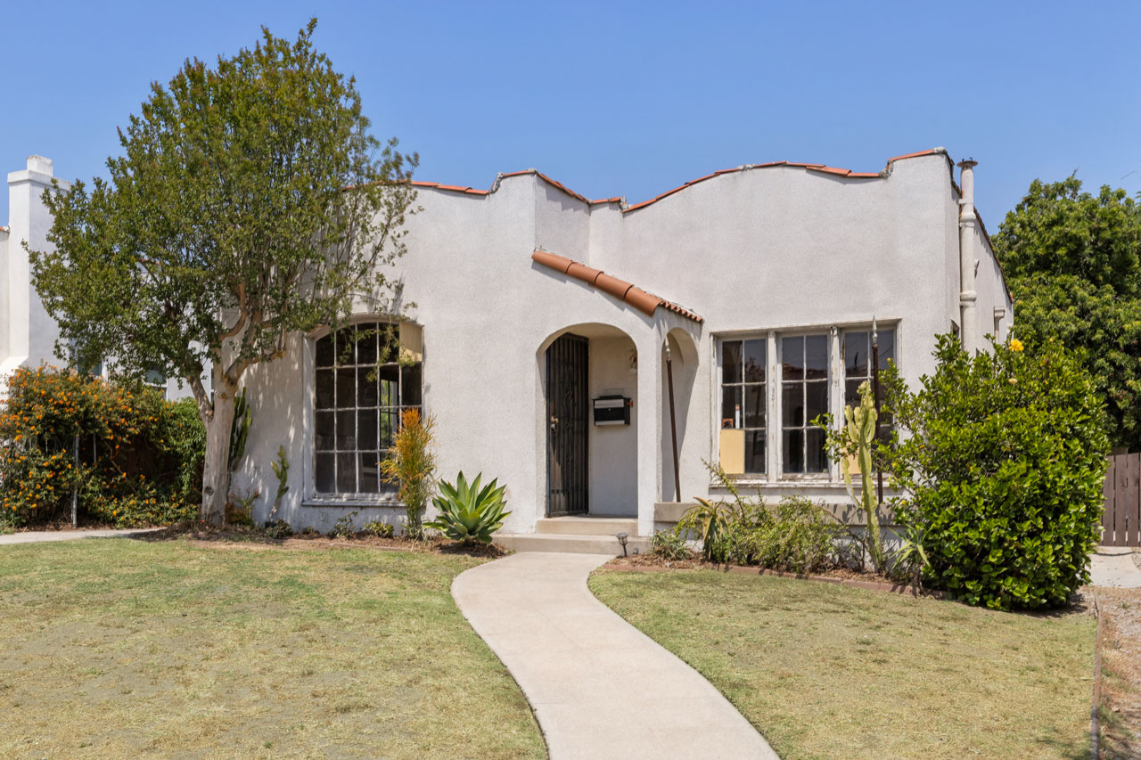 exterior of a one story spanish style home painted white with tile roof and grassy front yard