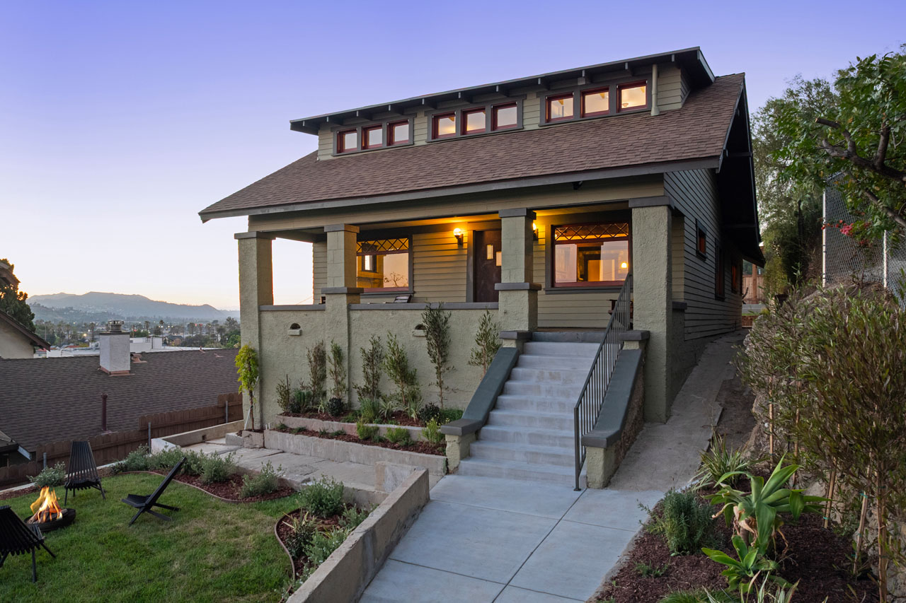 twilight exterior of a craftsman home painted live green with burn sienna trim and a grass yard with firepit