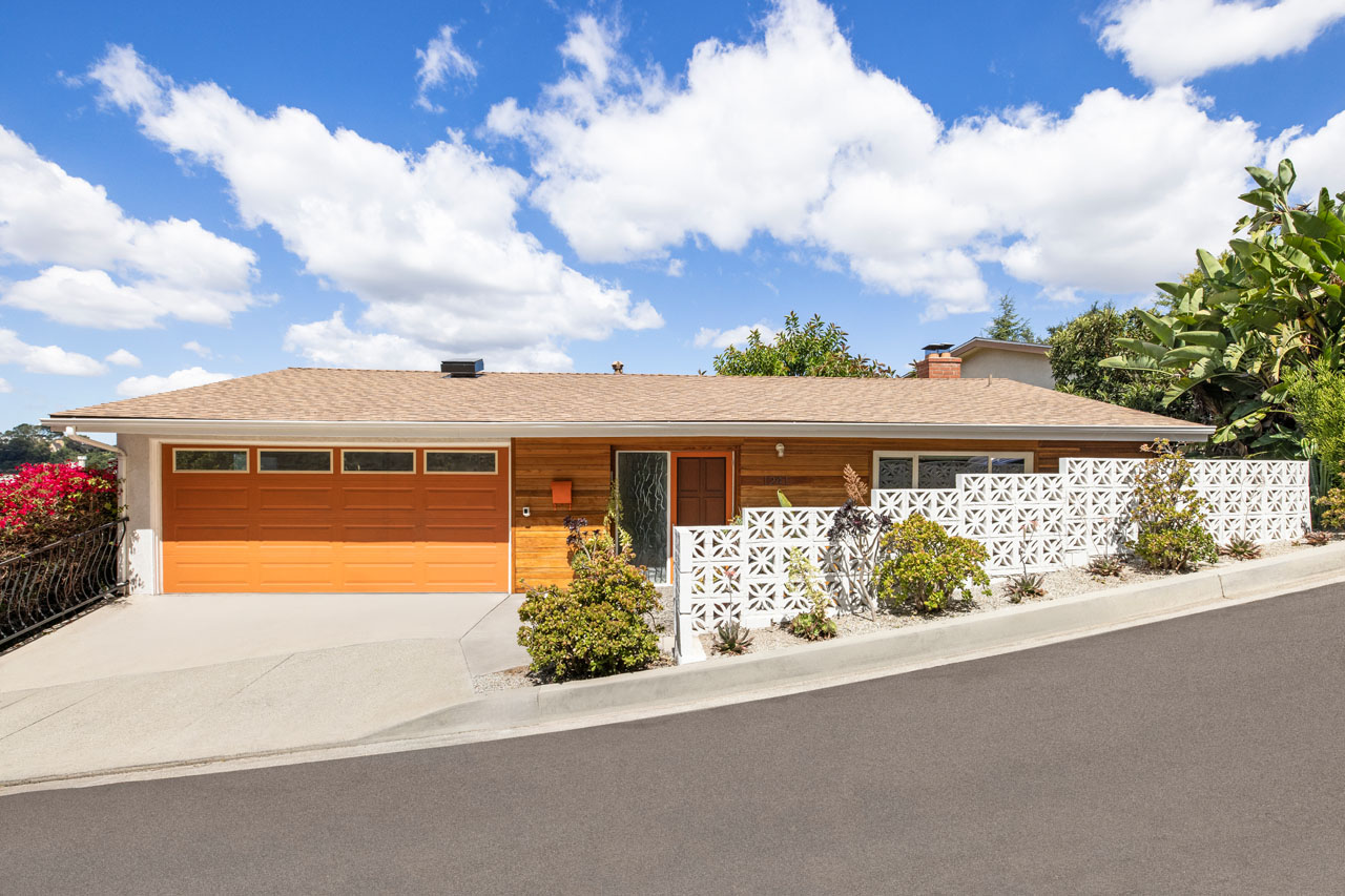exterior of a mid-century modern home painted orange and beige with a beautiful blue sky with fluffy clouds