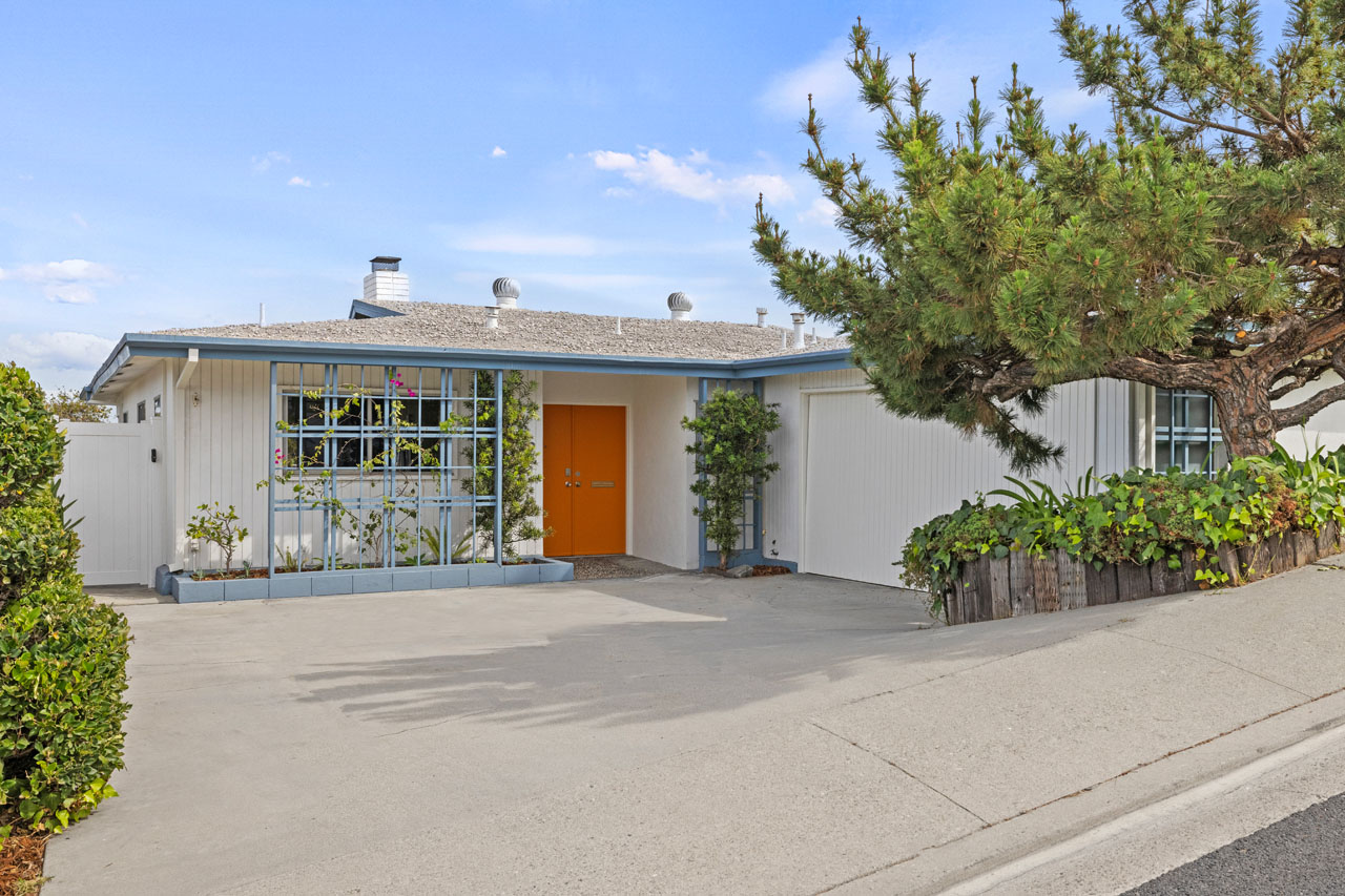 exterior of a one story mid-century style home painted white with blue trim and an orange front door