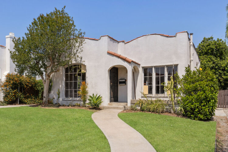 exterior of a one story spanish style home painted white with tile roof and grassy front yard