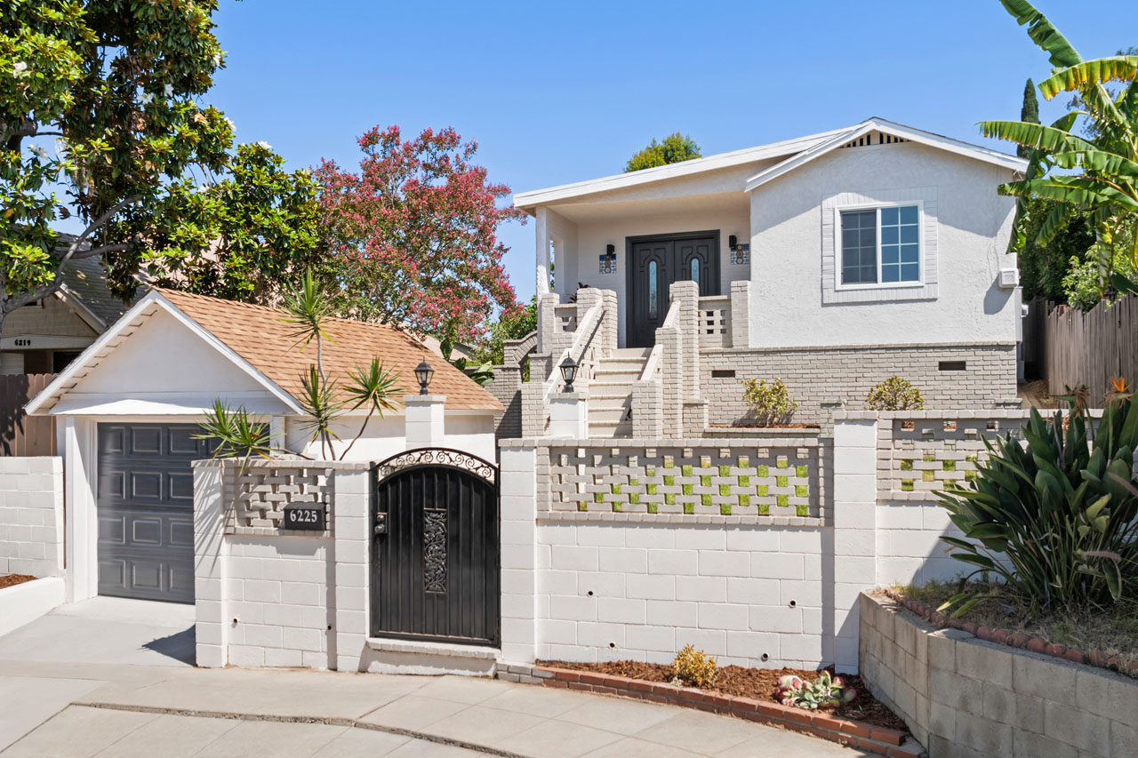 exterior of a traditional home on a hill, up from the street with a garage, all painted white and beige