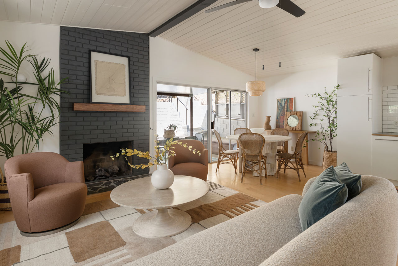 interior of a living room with fireplace couch, dining area and white ceiling with black wood beams