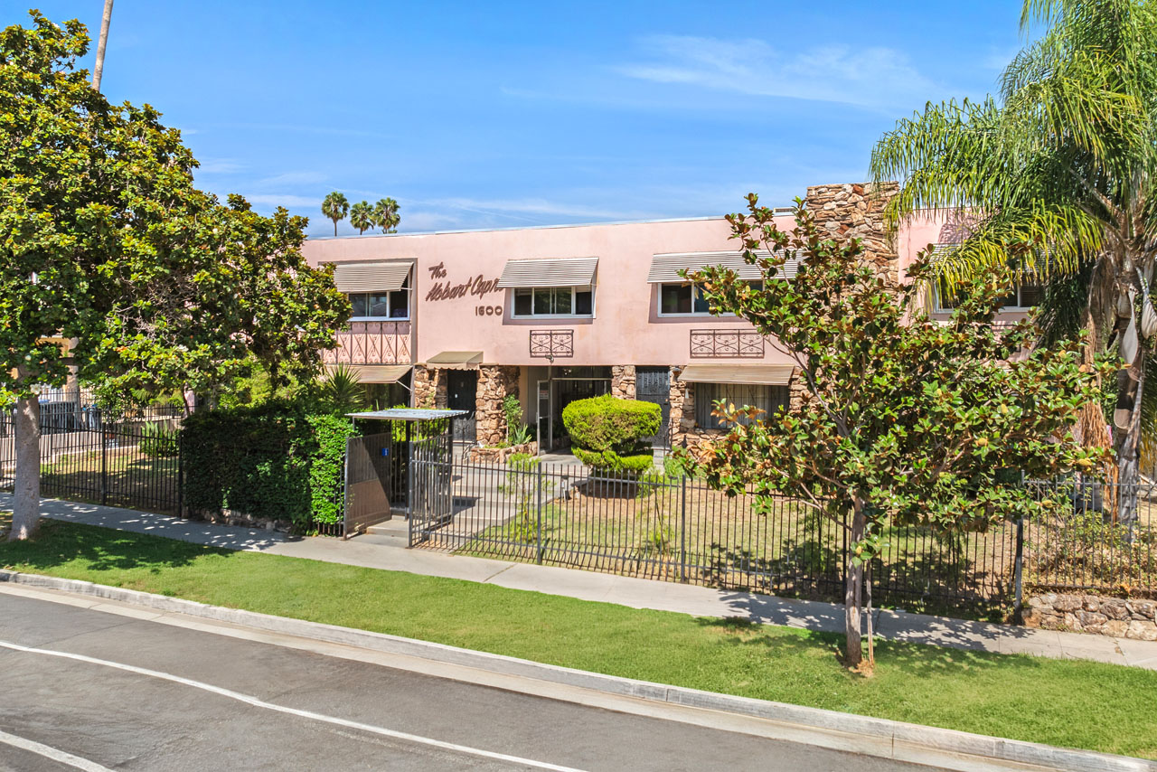 exterior of a pink two-story mid-century condo building with green grass and trees