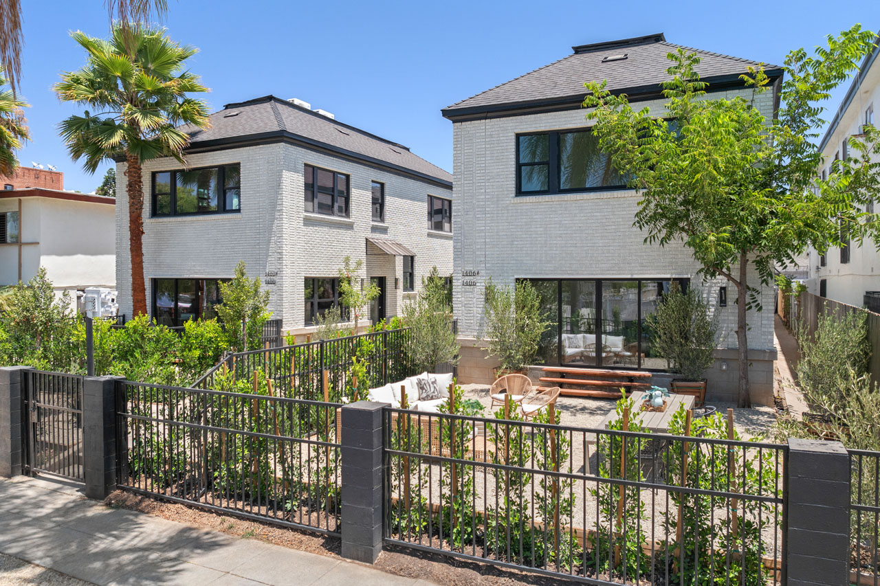 exterior of a two story tic building in white brick with drought tolerant landscaping and a black metal front fence and gate