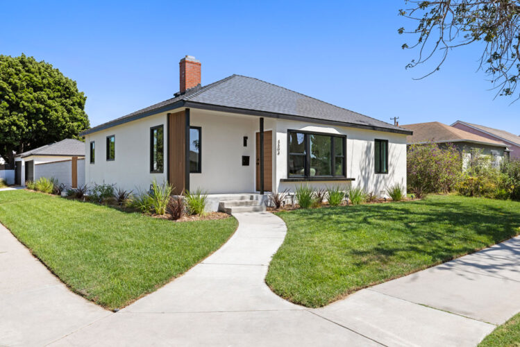 exterior of a traditional home updated with a contemporary look, painted white with black trim, green front yard and a red brick fireplace