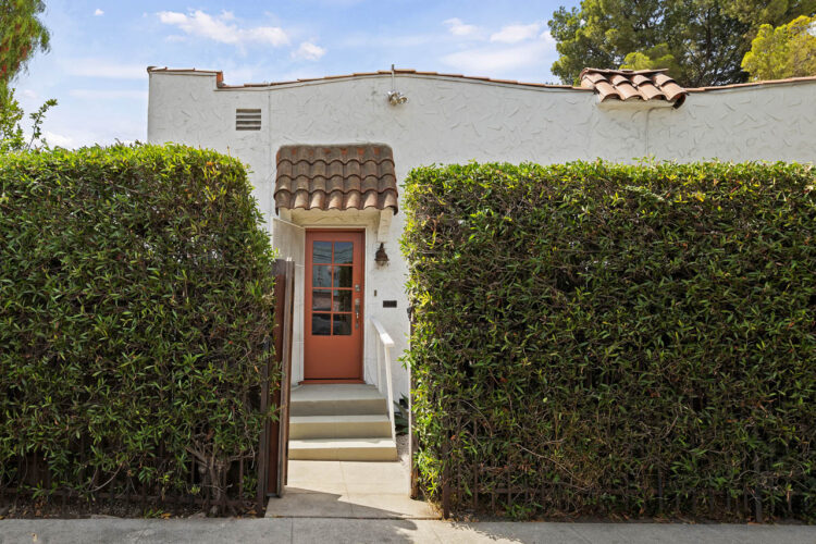 exterior of a spanish style casita condo with green hedge and orange gate