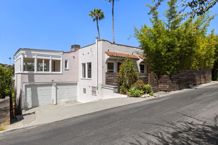 exterior of a spanish style duplex painted grey with saltillo roof and white details and garage doors, palm trees in background