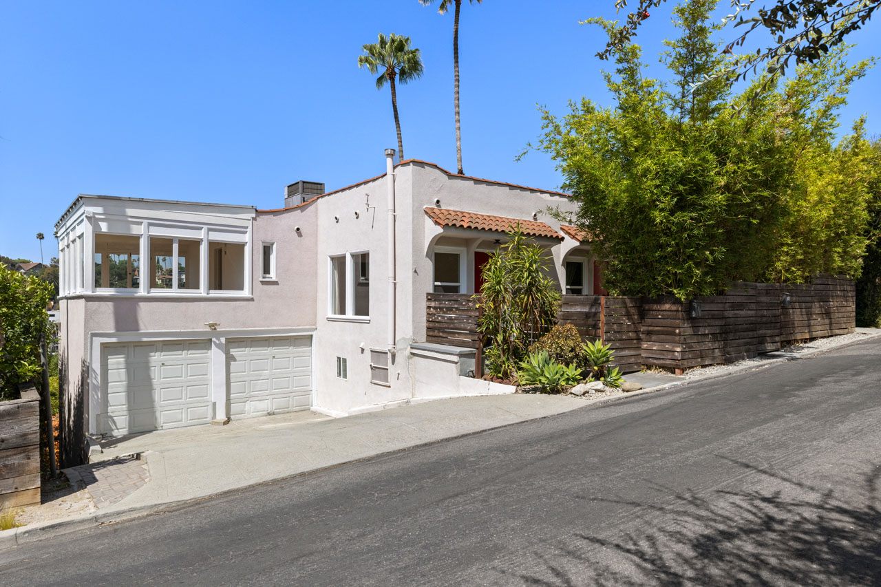 exterior of a spanish style duplex painted grey with saltillo roof and white details and garage doors, palm trees in background