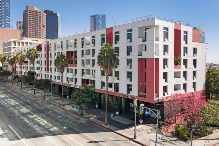 1234 Wilshire Blvd #115 Los Angeles 90017 exterior of a a six story condo building painted white and red with an empty road and palm trees