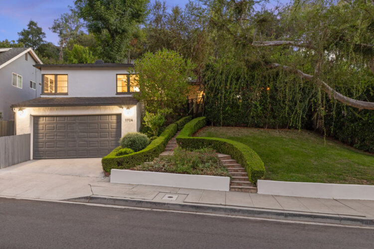 11704 Sunshine Ter Studio City twilight image of a traditional home with verdant surroundings a tree and boxwood hedges following a staircase up to the house